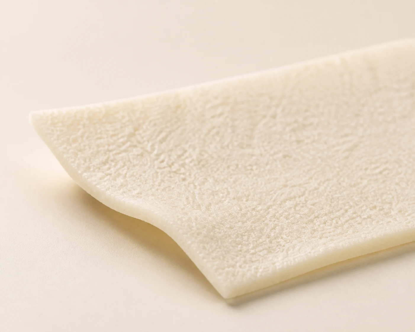 Close detail of a pale dermal matrix sheet with a gently curved edge
